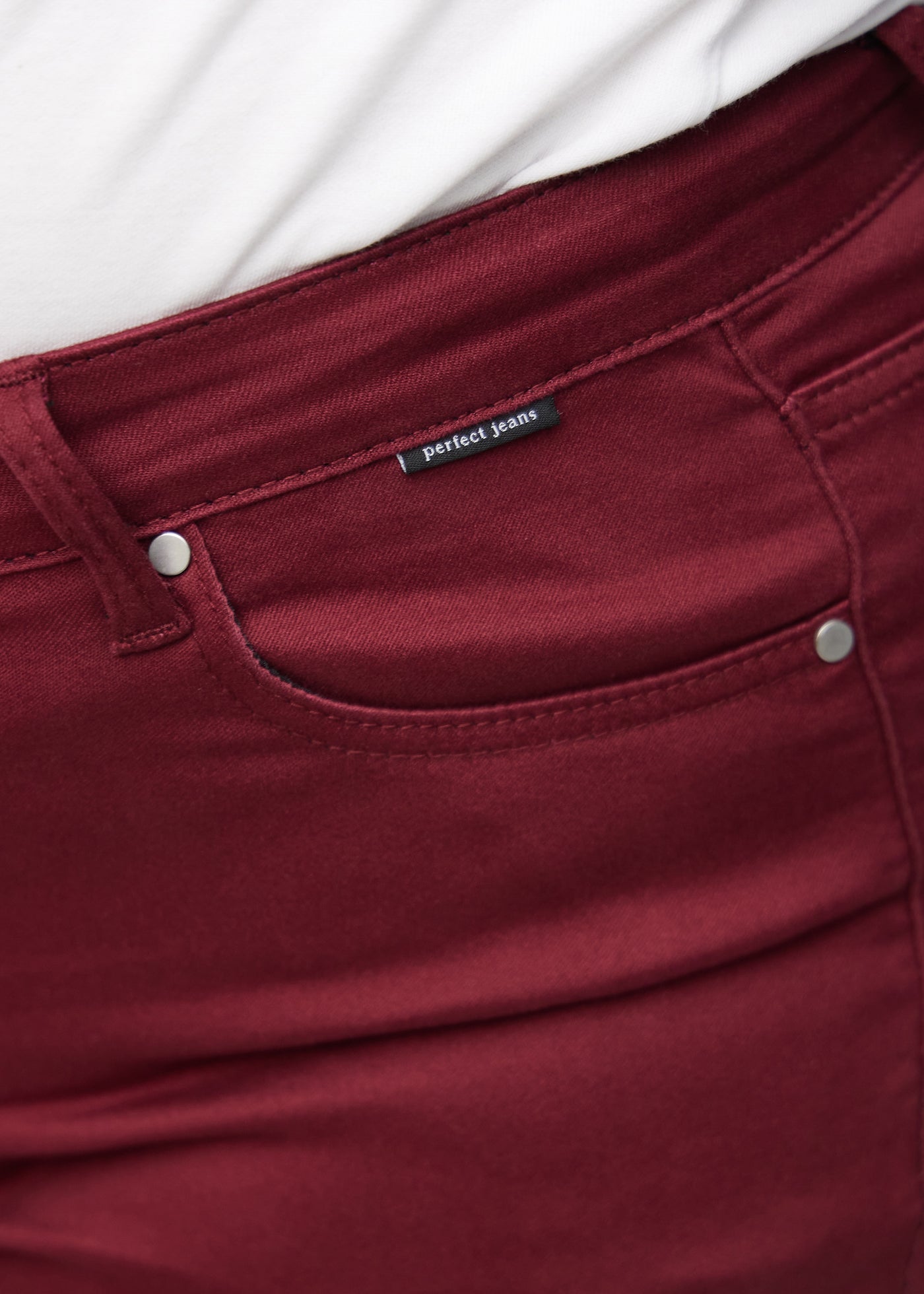 Forlommen på et par mørkerøde jeans, hvor man kan se logoet på en plus-size model.